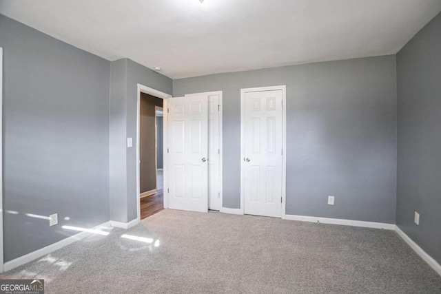 unfurnished bedroom featuring carpet flooring, two closets, and baseboards