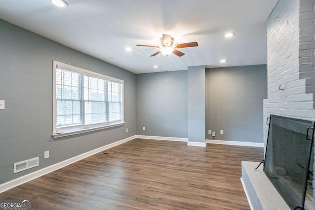 unfurnished living room with dark wood-style floors, visible vents, a brick fireplace, and baseboards