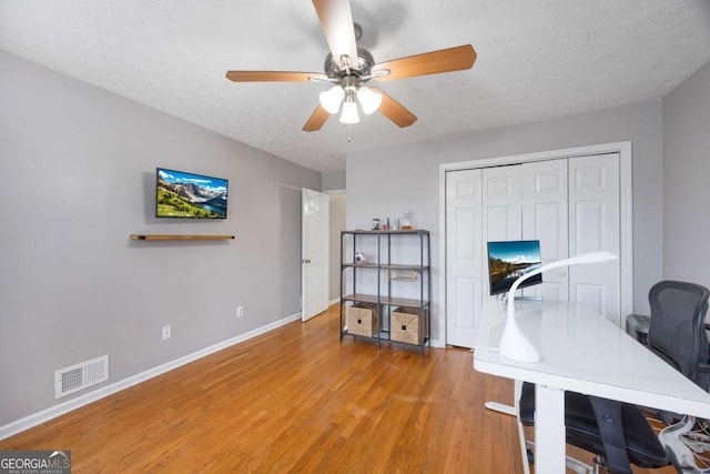 office area with visible vents, a textured ceiling, wood finished floors, baseboards, and ceiling fan