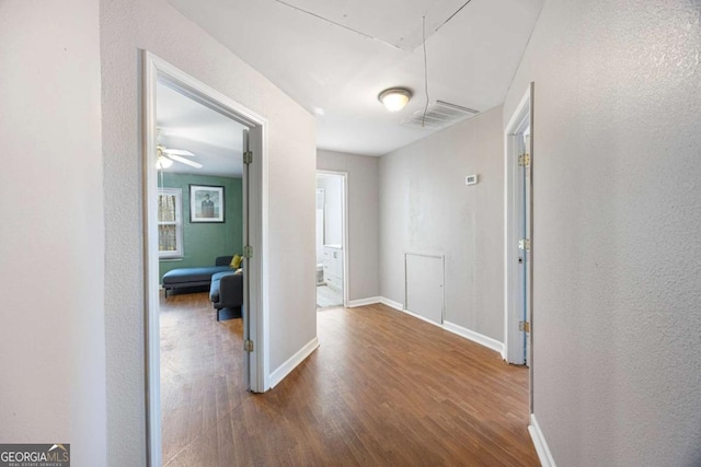 hallway with visible vents, baseboards, attic access, and wood finished floors