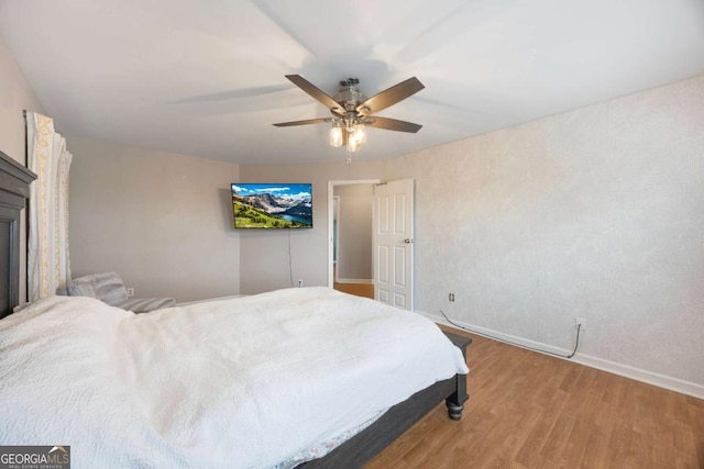 bedroom with light wood-type flooring, baseboards, a glass covered fireplace, and a ceiling fan