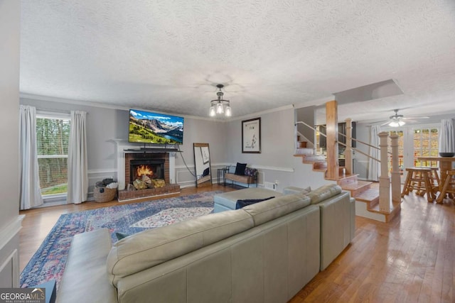 living area with ornamental molding, a textured ceiling, wood finished floors, a fireplace, and stairs