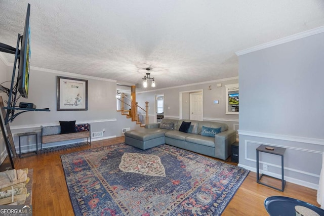 living area featuring stairway, wood finished floors, visible vents, a textured ceiling, and crown molding