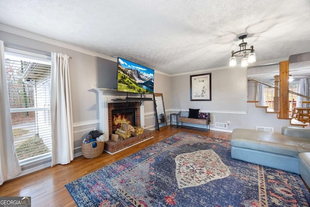 living area with a textured ceiling, a brick fireplace, wood finished floors, and crown molding