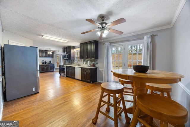 dining room featuring light wood-style floors, ornamental molding, a ceiling fan, and a textured ceiling