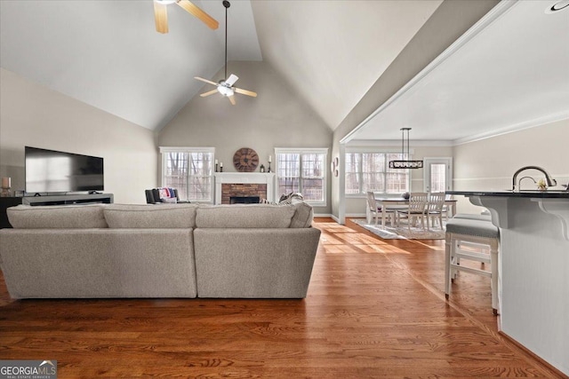 living area featuring baseboards, a stone fireplace, wood finished floors, high vaulted ceiling, and a ceiling fan