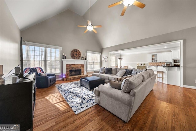 living area with a fireplace, high vaulted ceiling, ceiling fan, and wood finished floors