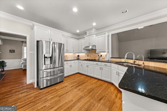 kitchen with crown molding, under cabinet range hood, light wood-type flooring, stainless steel fridge, and a sink