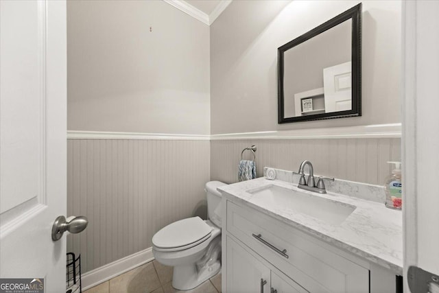 half bath with vanity, tile patterned flooring, wainscoting, crown molding, and toilet