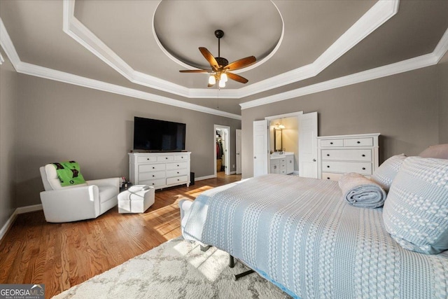 bedroom featuring a raised ceiling, a spacious closet, wood finished floors, and ornamental molding