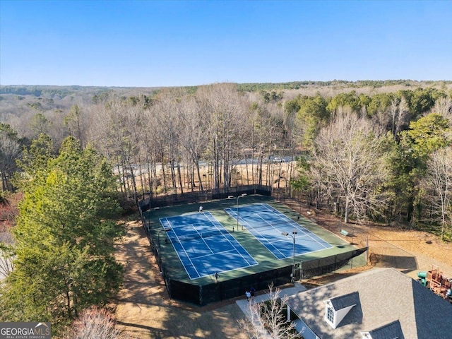 exterior space with a tennis court, a forest view, and fence