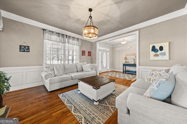 living area with wainscoting, wood finished floors, crown molding, and a decorative wall