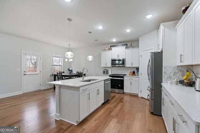 kitchen with an island with sink, a sink, light wood-style floors, appliances with stainless steel finishes, and white cabinetry