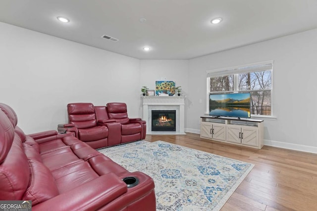 living room featuring a glass covered fireplace, recessed lighting, visible vents, and light wood finished floors