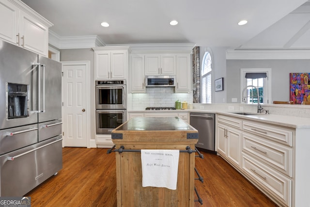 kitchen with a peninsula, a sink, ornamental molding, stainless steel appliances, and backsplash