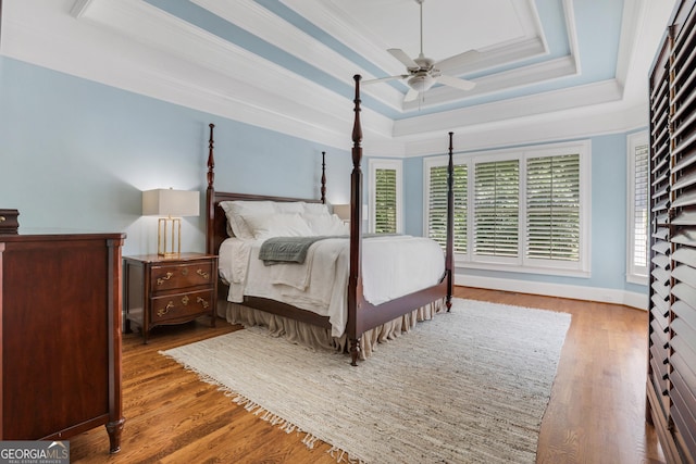 bedroom featuring a tray ceiling, crown molding, wood finished floors, and ceiling fan