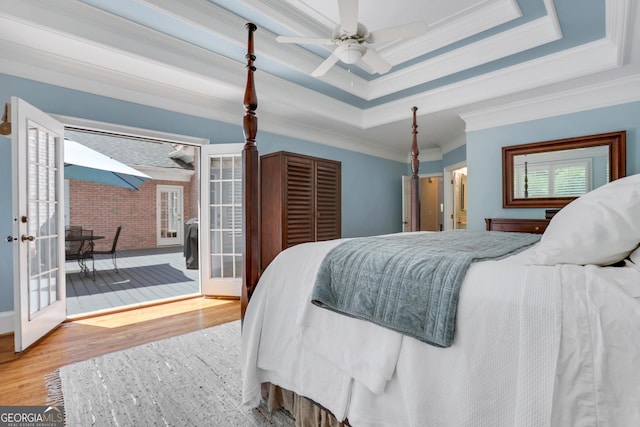 bedroom with a raised ceiling, crown molding, wood finished floors, and french doors