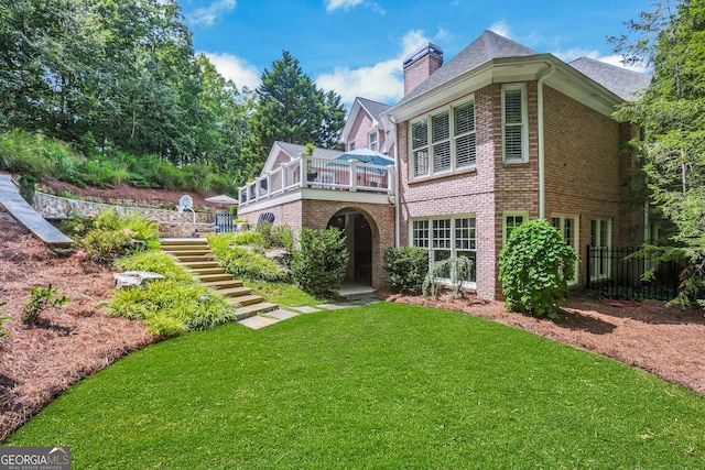 rear view of house featuring brick siding, stairway, a chimney, and a yard