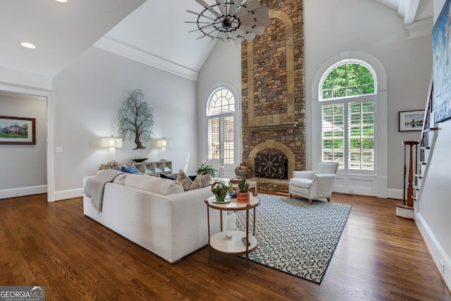 living area with stairway, high vaulted ceiling, a stone fireplace, and wood finished floors