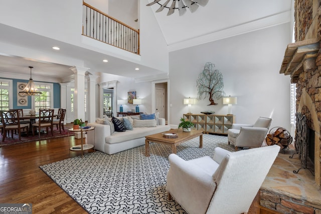 living room featuring wood finished floors, a fireplace, crown molding, decorative columns, and a towering ceiling