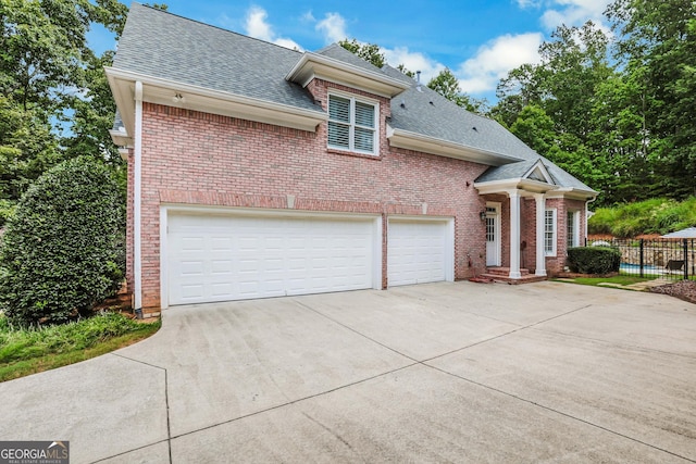 traditional home featuring brick siding, a shingled roof, fence, concrete driveway, and a garage