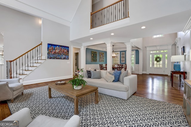 living area featuring wood finished floors, an inviting chandelier, decorative columns, stairs, and a towering ceiling