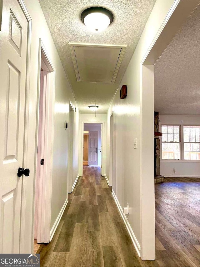 hallway with attic access, wood finished floors, and a textured ceiling