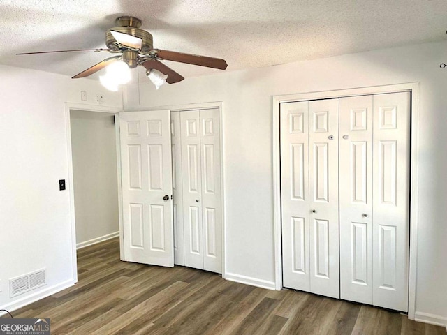 unfurnished bedroom featuring visible vents, multiple closets, dark wood-type flooring, and a textured ceiling