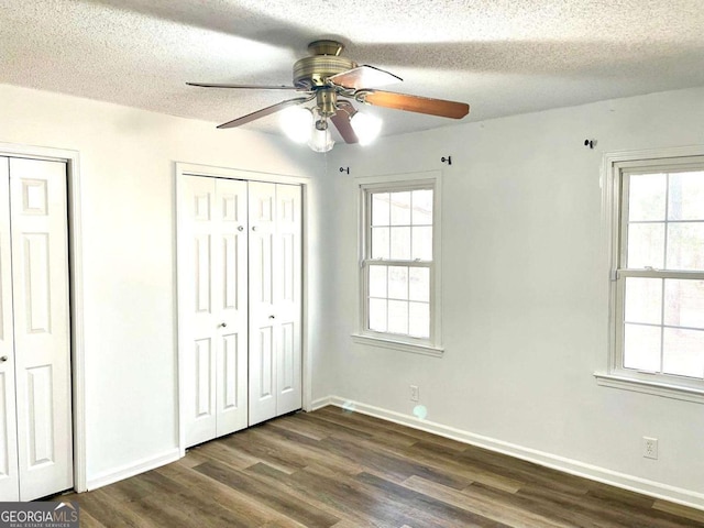 unfurnished bedroom featuring dark wood finished floors, baseboards, two closets, and a textured ceiling