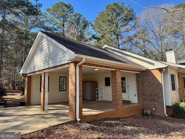 view of home's exterior with an attached carport, brick siding, a chimney, and driveway