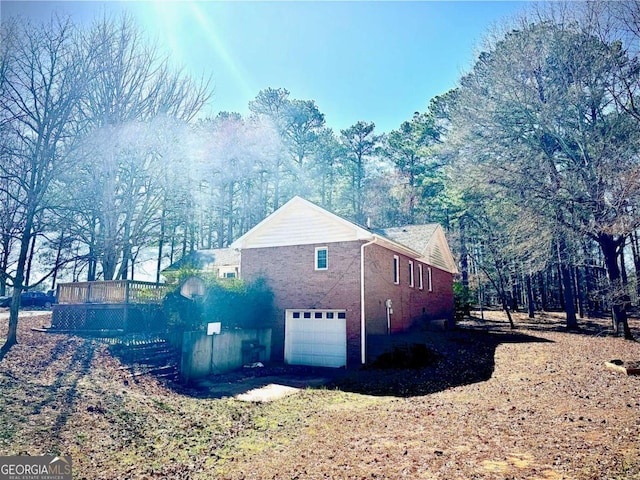 view of side of property featuring a garage, brick siding, and a wooden deck