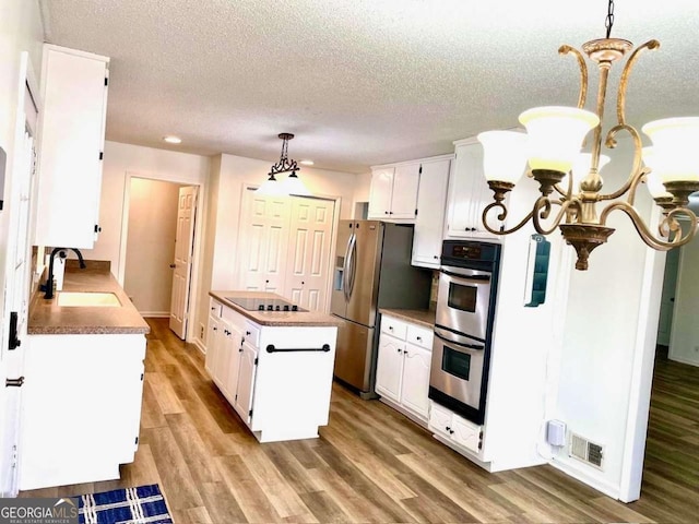 kitchen featuring visible vents, a sink, stainless steel appliances, a notable chandelier, and a center island