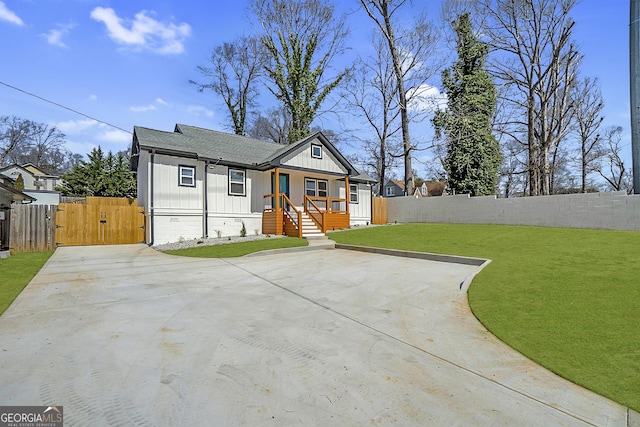 view of front facade with board and batten siding, a front lawn, fence, a porch, and a gate