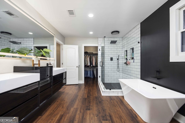 bathroom with wood finished floors, a freestanding bath, a shower stall, double vanity, and visible vents