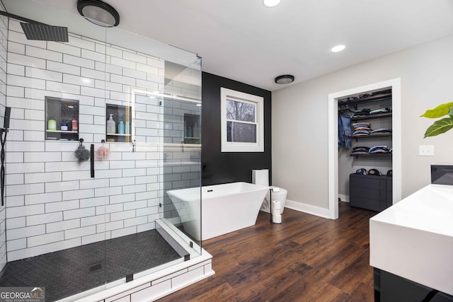 full bathroom featuring recessed lighting, wood finished floors, a freestanding bath, a shower stall, and baseboards