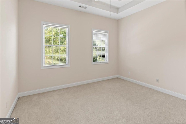 carpeted empty room with visible vents, a raised ceiling, and baseboards