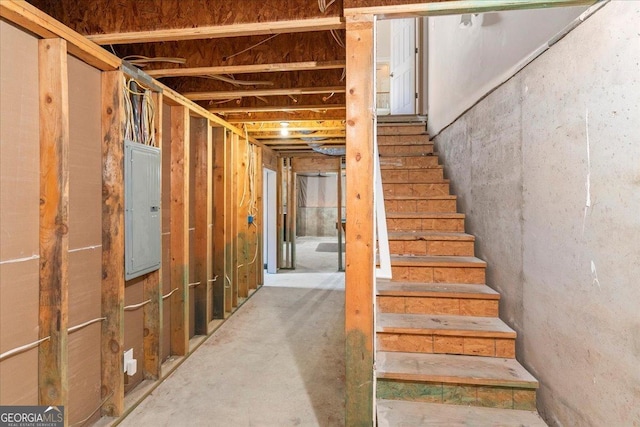 unfinished basement featuring stairs and electric panel