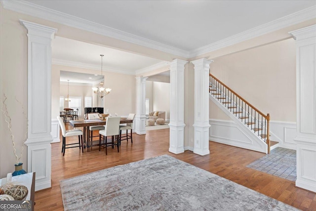 dining area featuring stairs, decorative columns, an inviting chandelier, wood finished floors, and a decorative wall