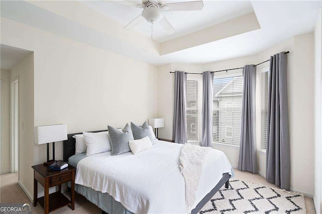 bedroom featuring a raised ceiling, a ceiling fan, baseboards, and light carpet