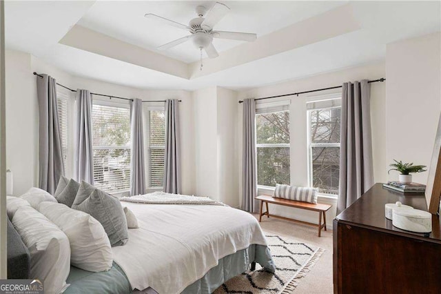 bedroom with light colored carpet, a raised ceiling, and a ceiling fan