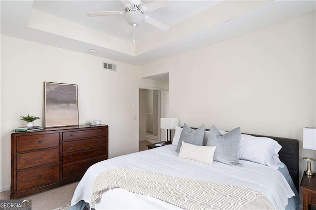 bedroom with a tray ceiling, visible vents, a ceiling fan, and carpet flooring