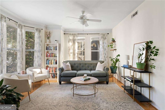 living room featuring wood finished floors, a ceiling fan, visible vents, and ornamental molding