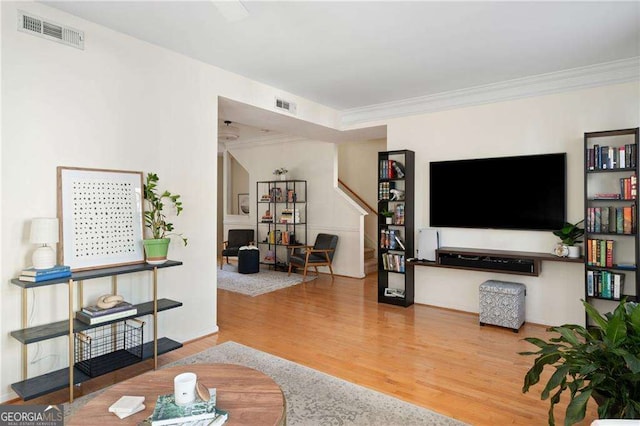 living area with visible vents, wood finished floors, and crown molding