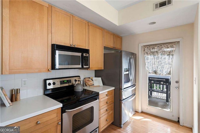 kitchen featuring visible vents, light wood-style flooring, stainless steel appliances, decorative backsplash, and light countertops