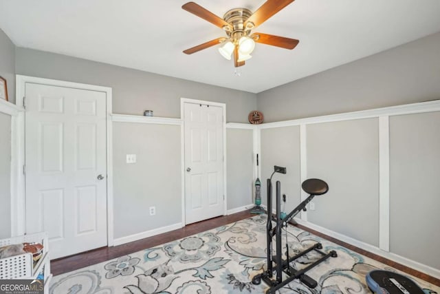 exercise room with a ceiling fan, baseboards, and wood finished floors