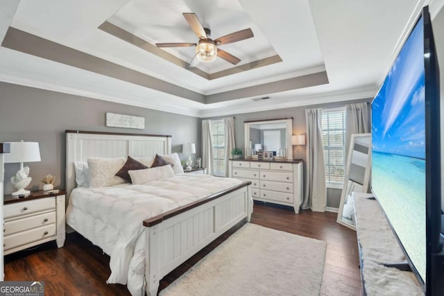 bedroom featuring visible vents, crown molding, a tray ceiling, dark wood-style floors, and a ceiling fan