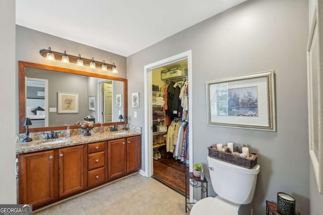 full bath featuring double vanity, a spacious closet, toilet, and a sink