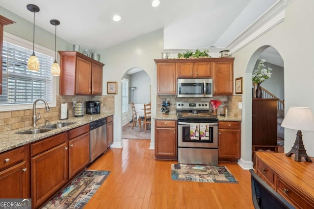 kitchen with arched walkways, a sink, hanging light fixtures, light wood-style floors, and appliances with stainless steel finishes