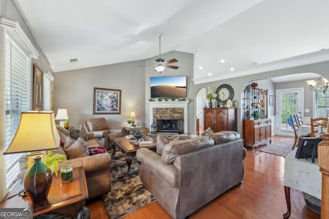 living area with visible vents, lofted ceiling, ceiling fan with notable chandelier, a fireplace, and wood finished floors