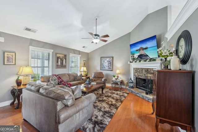 living room with wood finished floors, visible vents, a ceiling fan, lofted ceiling, and a stone fireplace